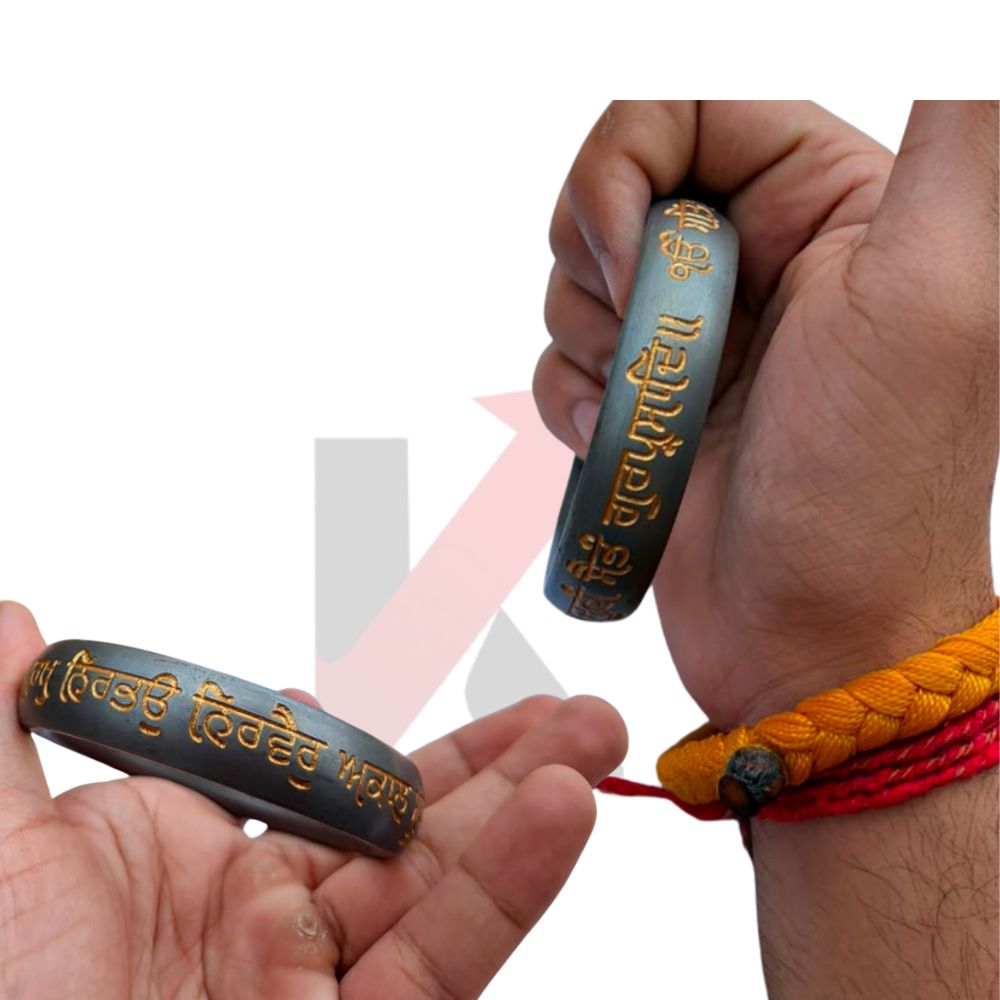 Two dark gray metallic bracelets with gold Punjabi script, shown being held by hands against a white background. One bracelet is displayed on a wrist alongside an orange and red braided cord . bracelet.